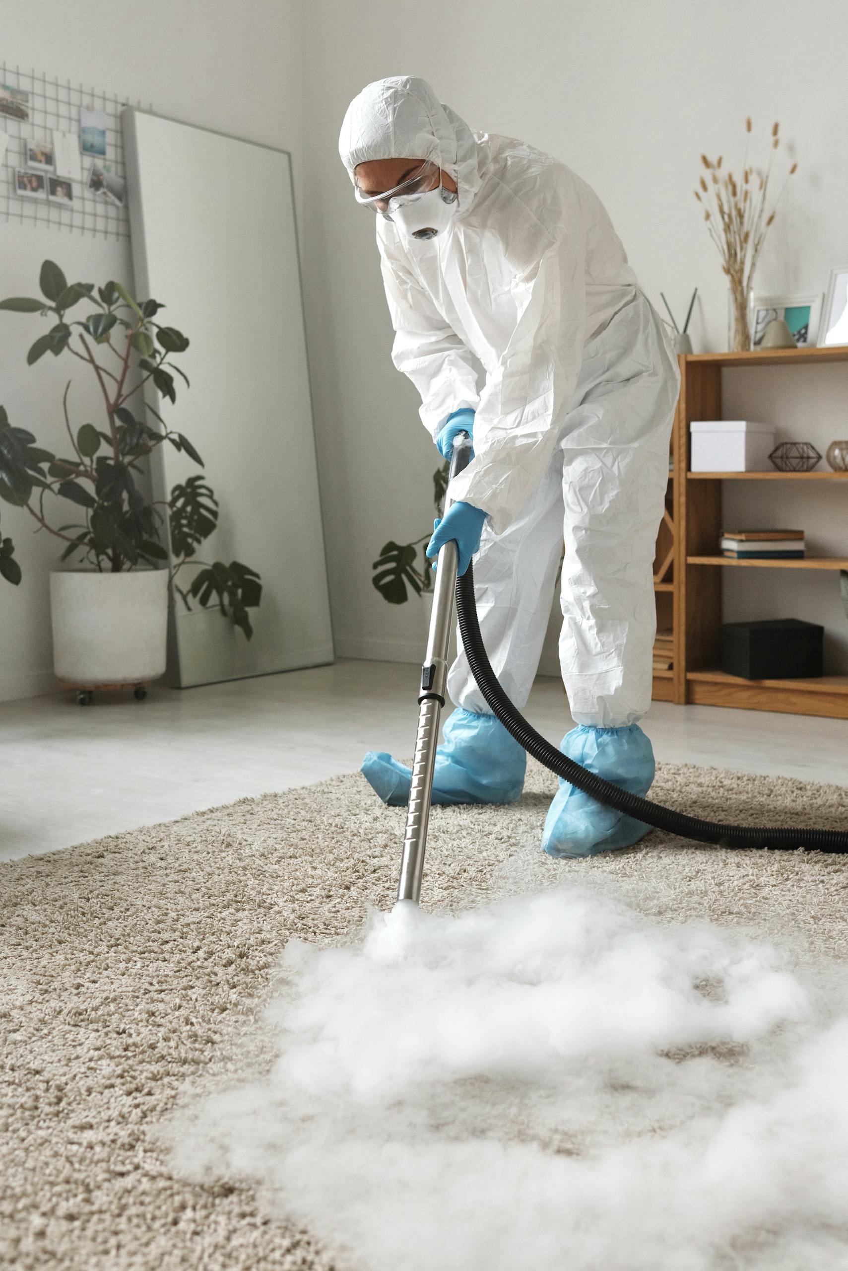 A Woman in a Protective Suit Disinfecting a Carpet